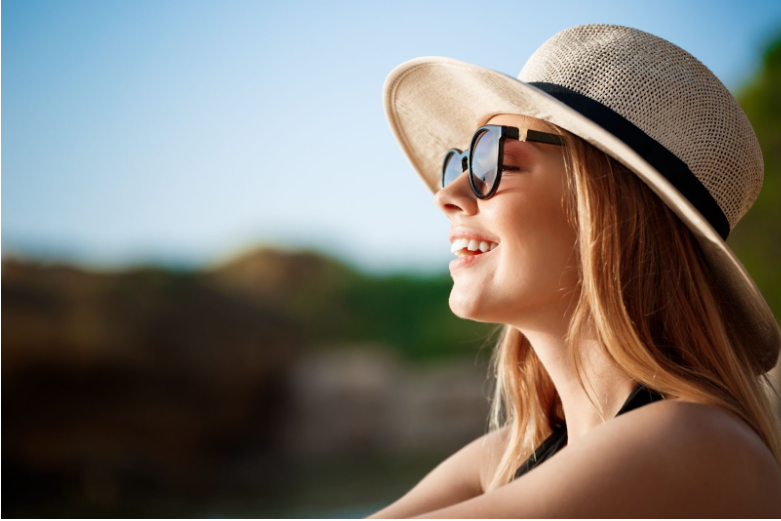 Жена носи шапка и слънчеви очила като защита против фотостареене